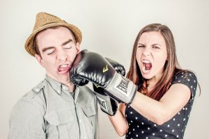 Image humoristique d'une femme donnant un faux coup de poing avec un gant de boxe a un homme mince en chemise avec un chapeau